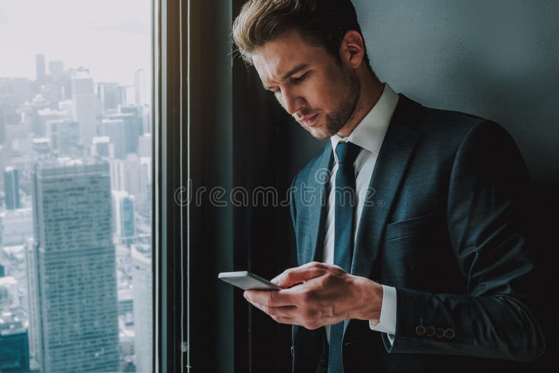 Młoda przedsiębiorca pozycja blisko używać smartphone i okno zdjęcia stock Młoda przedsiębiorca pozycja blisko używać smartphone i okno zdjęcia stock
