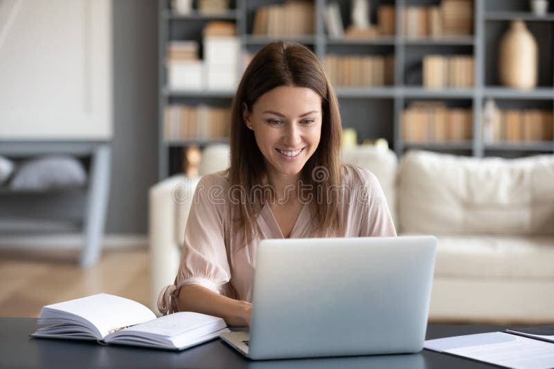 Head shot young happy woman sitting at desk, working on computer at home. Pleasant attractive smiling lady looking at laptop screen, shopping, chatting in social networks, studying online remotely. Head shot young happy woman sitting at desk, working on computer at home. Pleasant attractive smiling lady looking at laptop screen, shopping, chatting in social networks, studying online remotely.