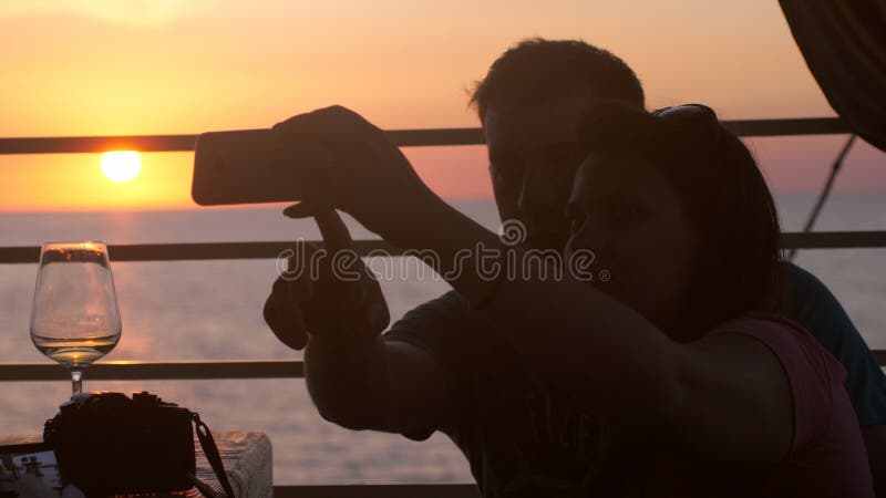 Młoda szczęśliwa para w miłości bierze selfie fotografię z telefonem komórkowym w plażowej kawiarni podczas pięknego zmierzchu i zdjęcie royalty free Młoda szczęśliwa para w miłości bierze selfie fotografię z telefonem komórkowym w plażowej kawiarni podczas pięknego zmierzchu i zdjęcie royalty free