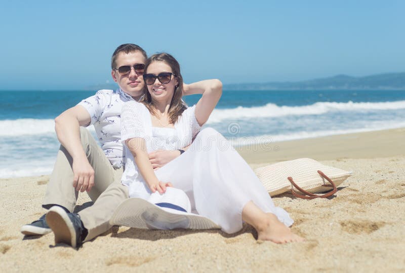 Młoda uśmiechnięta para siedzi na plaży w okularach przeciwsłonecznych obrazy stock Młoda uśmiechnięta para siedzi na plaży w okularach przeciwsłonecznych obrazy stock