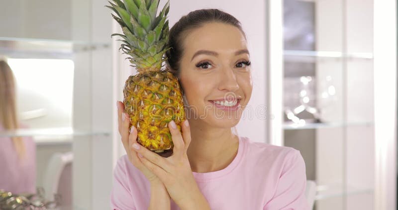 Młoda śmieszna kobieta bawić się z ananasem na kuchni