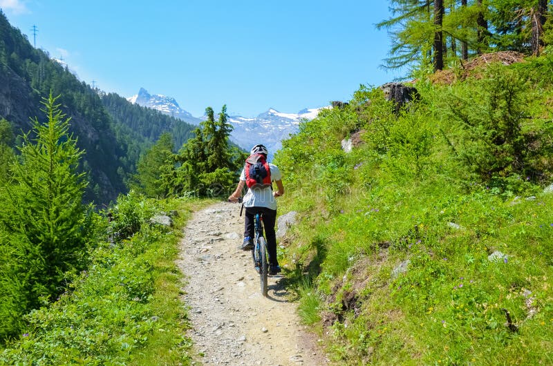 Młodego człowieka jeździecki bicykl w pięknym górkowatym krajobrazie Szwajcarscy Alps blisko do sławnego Zermatt na terenach odkr zdjęcia stock Młodego człowieka jeździecki bicykl w pięknym górkowatym krajobrazie Szwajcarscy Alps blisko do sławnego Zermatt na terenach odkr zdjęcia stock