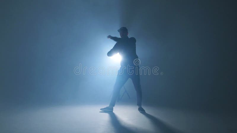 Młodego człowieka tancerz tanczy ostrego hip hop na odosobnionym pracownianym neonowym błękitnym tle, zwolnione tempo