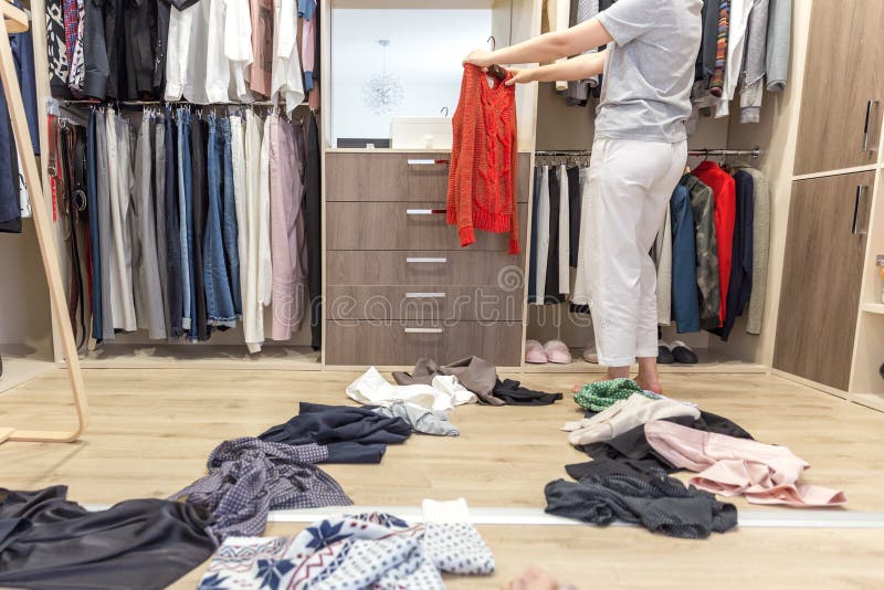 Young woman throwing clothes in walk in closet. Mess in wardrobe and dressing room concept. Young woman throwing clothes in walk in closet. Mess in wardrobe and dressing room concept