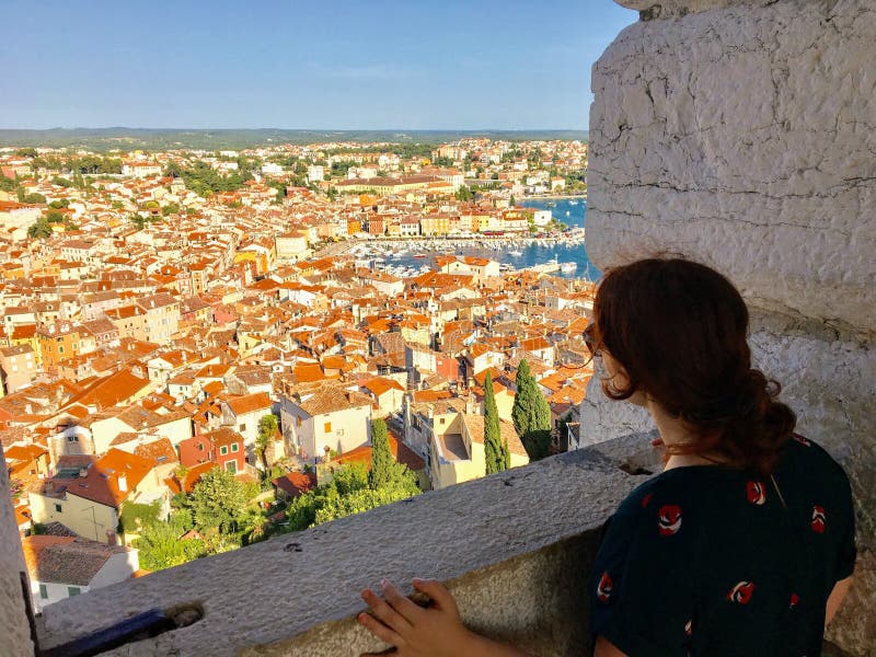 Młodej kobiety samotna pozycja z wierzchu stary kamienny dzwonkowy wierza przyglądający za pięknym starym miasteczku Rovinj przy, fotografia royalty free Młodej kobiety samotna pozycja z wierzchu stary kamienny dzwonkowy wierza przyglądający za pięknym starym miasteczku Rovinj przy, fotografia royalty free