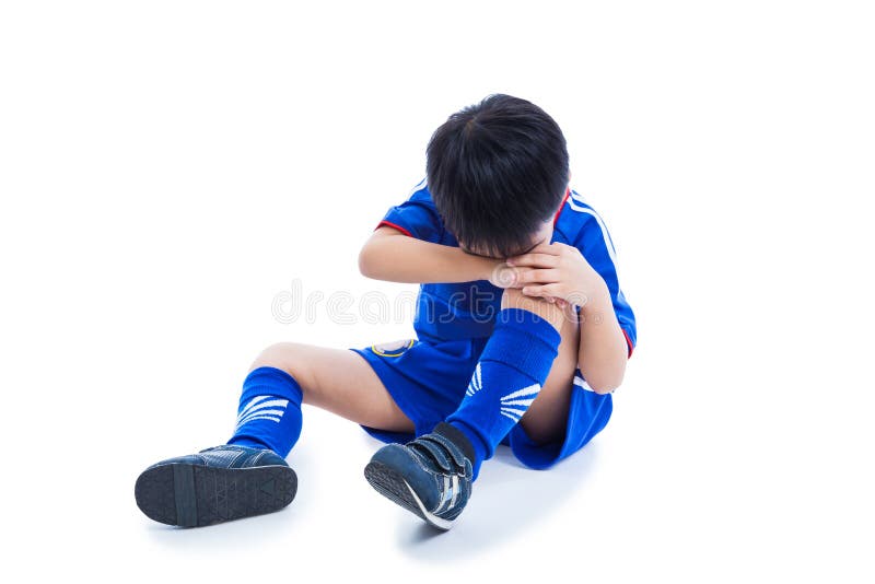 Sports injury. Youth asian &#x28;thai&#x29; soccer player in blue uniform with pain in knee. Isolated on white background. Studio shot. Full body. Boy sitting and crying. Sports injury. Youth asian &#x28;thai&#x29; soccer player in blue uniform with pain in knee. Isolated on white background. Studio shot. Full body. Boy sitting and crying.