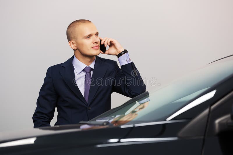 Młody biznesowy mężczyzna dzwoni na telefonie przy samochodem zdjęcie stock Młody biznesowy mężczyzna dzwoni na telefonie przy samochodem zdjęcie stock