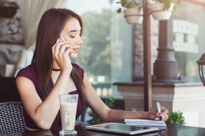 Młody bizneswoman opowiada na smartphone i robi notatkom obrazy royalty free Młody bizneswoman opowiada na smartphone i robi notatkom obrazy royalty free
