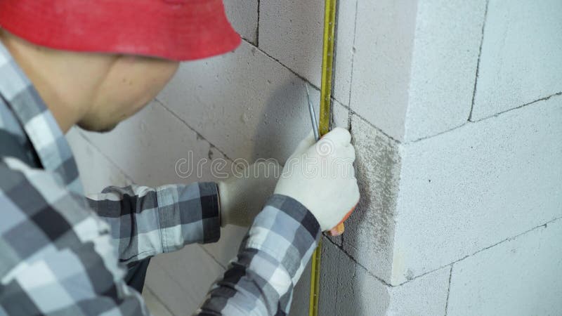 Młody budowniczy w pracy nosi zaciski mocujące i metalową szynę na ścianie bloku