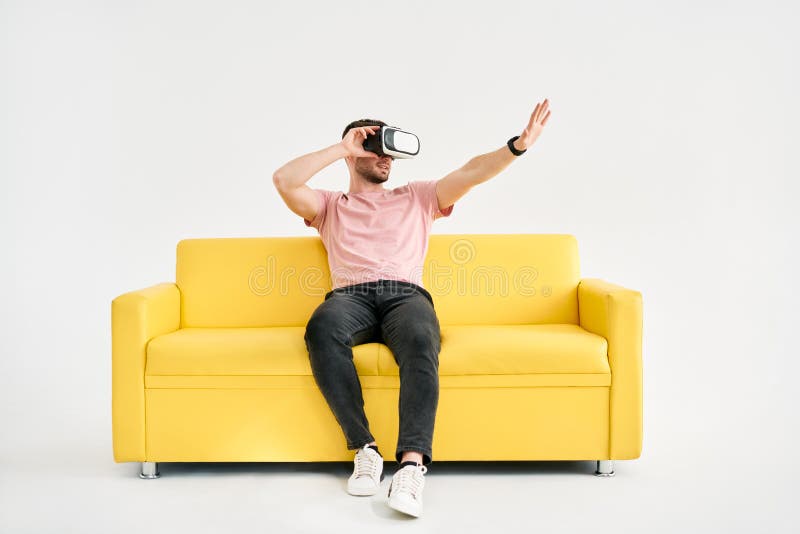 Młody człowiek w zestawie słuchawkowym wirtualnej rzeczywistości grający w gry wideo i próbujący dotknąć czegoś rękami