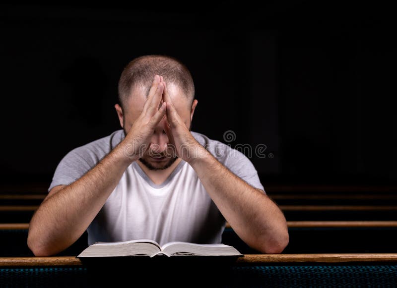 A young guy sits on a church bench, reads the bible and prays. The concept of religion, prayer, faith. A young guy sits on a church bench, reads the bible and prays. The concept of religion, prayer, faith.