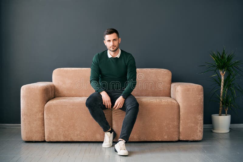 Młody modny mężczyzna siedzący na sofie, patrzący kamerą