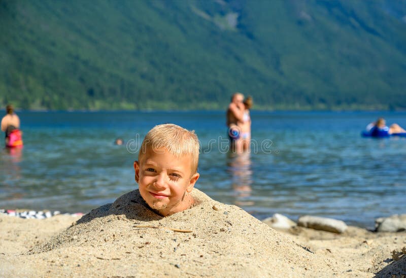 MÅ‚ody, niegrzeczny blondyn, kaukaski chÅ‚opiec na wakacjach leżący w piasku na plaży i caÅ‚e jego ciaÅ‚o jest pokryte fotografia royalty free MÅ‚ody, niegrzeczny blondyn, kaukaski chÅ‚opiec na wakacjach leżący w piasku na plaży i caÅ‚e jego ciaÅ‚o jest pokryte fotografia royalty free