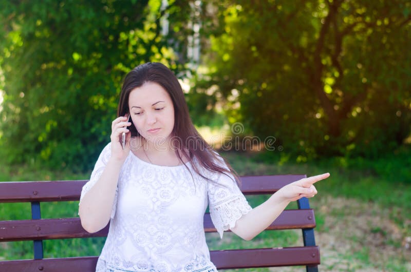 Młody piękny europejski dziewczyny obsiadanie na ławce i opowiadać na telefonie Dziewczyna wskazuje palcowy oddalonego, daje, rad zdjęcie royalty free Młody piękny europejski dziewczyny obsiadanie na ławce i opowiadać na telefonie Dziewczyna wskazuje palcowy oddalonego, daje, rad zdjęcie royalty free