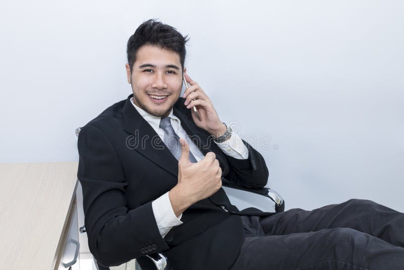 Młody przystojny biznesmen ono uśmiecha się i opowiada z telefonem przy biurem zdjęcia stock Młody przystojny biznesmen ono uśmiecha się i opowiada z telefonem przy biurem zdjęcia stock