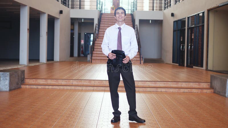 Młody przystojny uśmiechnięty biznesmen w kostiumu chodzi z teczki spojrzeniami przy kamerą w biznesowym centre Komunikacja zdjęcia royalty free Młody przystojny uśmiechnięty biznesmen w kostiumu chodzi z teczki spojrzeniami przy kamerą w biznesowym centre Komunikacja zdjęcia royalty free