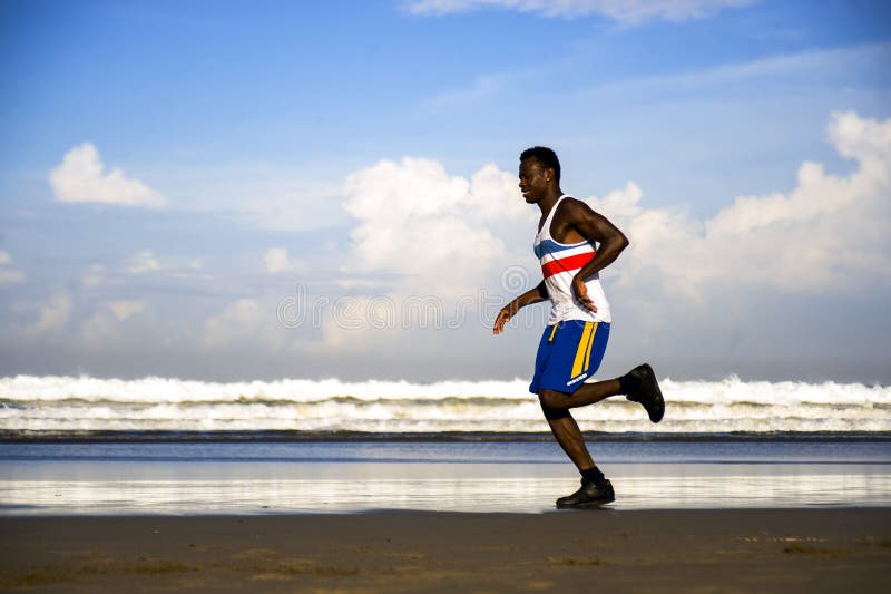 Healthy lifestyle portrait of young athletic and attractive black African American runner men doing running workout training on desert beach in fitness and wellness isolated on blue sky. Healthy lifestyle portrait of young athletic and attractive black African American runner men doing running workout training on desert beach in fitness and wellness isolated on blue sky