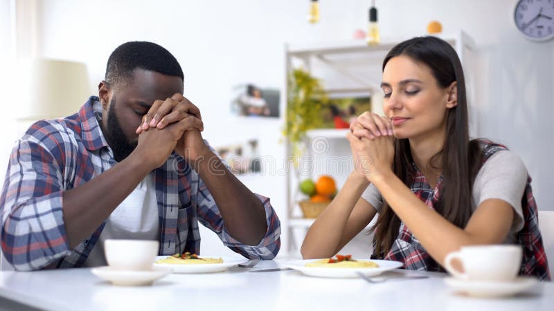 Young multiethnic couple praying before lunch, thanking God for meal, religion, stock photo. Young multiethnic couple praying before lunch, thanking God for meal, religion, stock photo