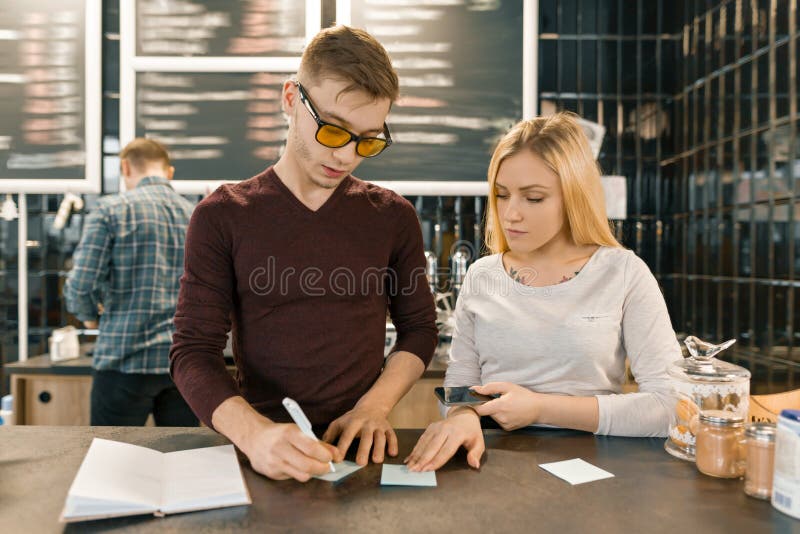 Młodzi ludzie pracuje w sklepu z kawą, mężczyzny i kobiety blisko barze odpierającym, odbiorczy rozkaz telefonem, barista na tle zdjęcie stock Młodzi ludzie pracuje w sklepu z kawą, mężczyzny i kobiety blisko barze odpierającym, odbiorczy rozkaz telefonem, barista na tle zdjęcie stock