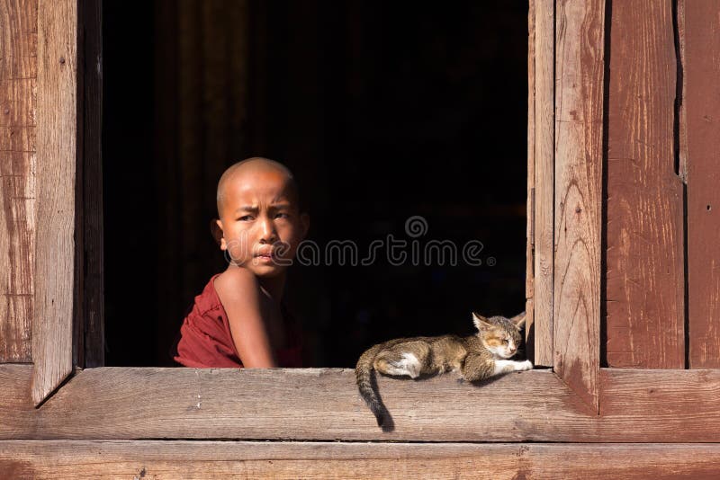 NYAUNG SHWE, MYANMAR, JANUARY 27, 2015 : A young novice buddhist monk is looking at the window of the Shwe Yaunghwe Kyaung monastery in Nyaung Shwe, Myanmar (Burma). NYAUNG SHWE, MYANMAR, JANUARY 27, 2015 : A young novice buddhist monk is looking at the window of the Shwe Yaunghwe Kyaung monastery in Nyaung Shwe, Myanmar (Burma).