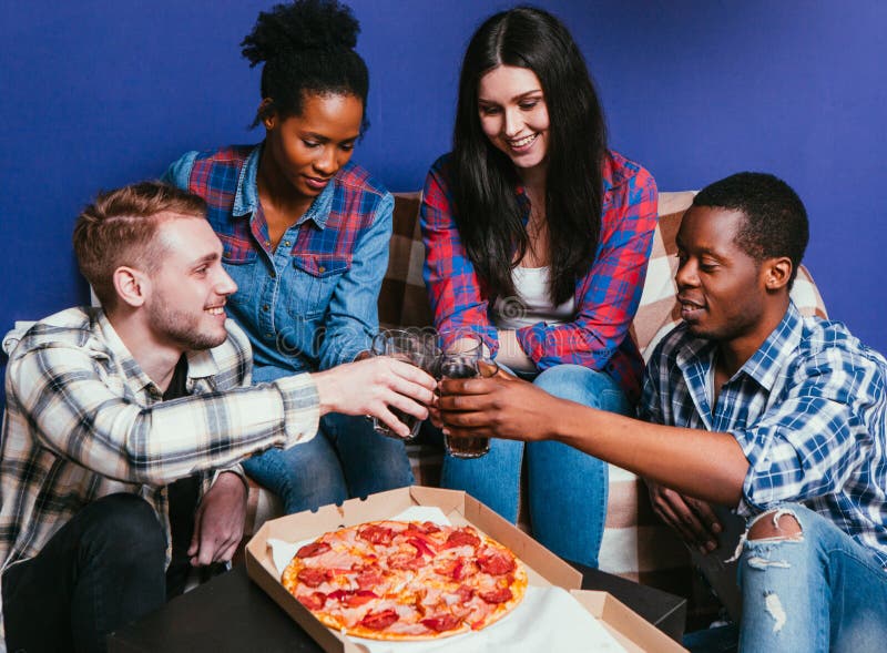 Young friends international company eat pizza with soda, cheers. Four happy people together, fun leisure, home party, unhealthy food concept. Young friends international company eat pizza with soda, cheers. Four happy people together, fun leisure, home party, unhealthy food concept.