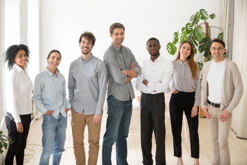 Young happy multiracial professionals or company staff looking at camera smiling, multi-ethnic group of diverse business people standing together, employees posing in office, successful team portrait. Young happy multiracial professionals or company staff looking at camera smiling, multi-ethnic group of diverse business people standing together, employees posing in office, successful team portrait