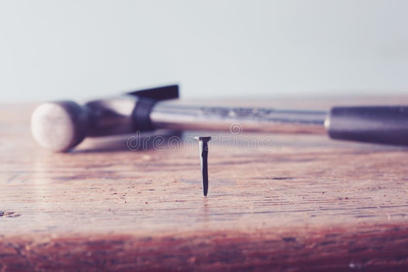 Close up on a nail in a table with hammer in background. Close up on a nail in a table with hammer in background