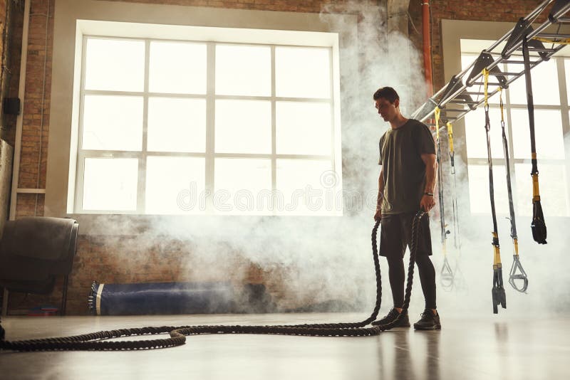 N'arrêtez pas. Vue de côté de jeune homme sportif avec le corps parfait à faire des exercices de crossfit avec une corde dans la s images stock
