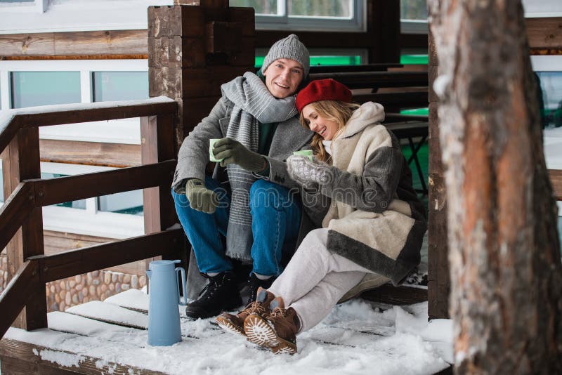 After spending a day off in the woods in winter, a young couple basks in a summer house and drinks a hot drink from mugs. After spending a day off in the woods in winter, a young couple basks in a summer house and drinks a hot drink from mugs.