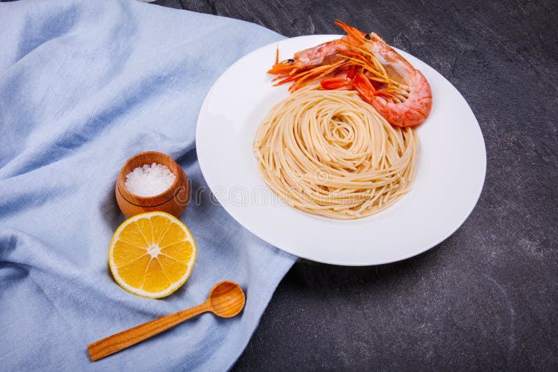 Na stole jest spaghetti z królewskimi krewetkami, plasterkiem cytryna i garnkiem, obraz royalty free Na stole jest spaghetti z królewskimi krewetkami, plasterkiem cytryna i garnkiem, obraz royalty free