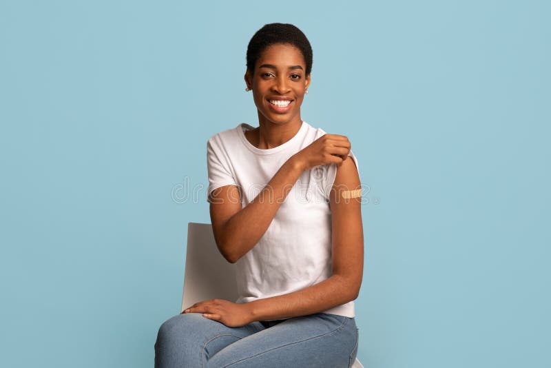 After Vaccination Concept. Portrait Of Vaccinated Black Woman Showing Arm After Coronavirus Vaccine Injection, Positive Lady Sitting With Rolled Up Sleeve Over Blue Background, Smiling To Camera. After Vaccination Concept. Portrait Of Vaccinated Black Woman Showing Arm After Coronavirus Vaccine Injection, Positive Lady Sitting With Rolled Up Sleeve Over Blue Background, Smiling To Camera