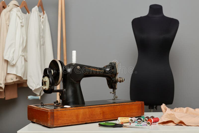 Seamstress workplace with sewing machine on table, needles, pins, threads, mannequin with new dress, hanger with sewn outfits. Seamstress workplace with sewing machine on table, needles, pins, threads, mannequin with new dress, hanger with sewn outfits.
