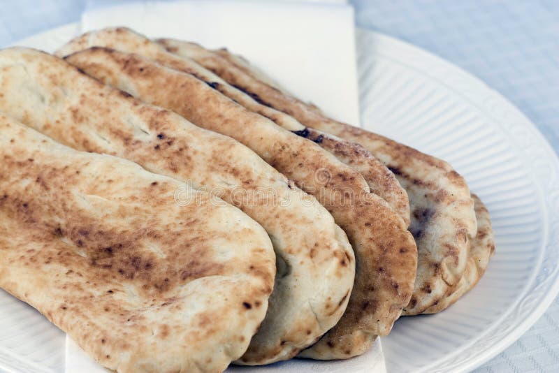 Fresh baked Naan bread on white plate Naan is an East Indian flat bread, traditionally baked in a Tandoor oven.