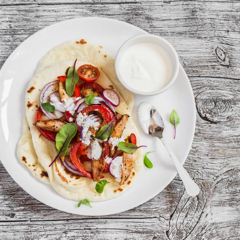 Naan bread with grilled chicken, red sweet peppers and yoghurt on a light wooden background