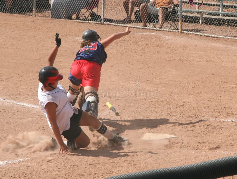 A young lady, or teen, crashing into the catcher as she slides home. A young lady, or teen, crashing into the catcher as she slides home