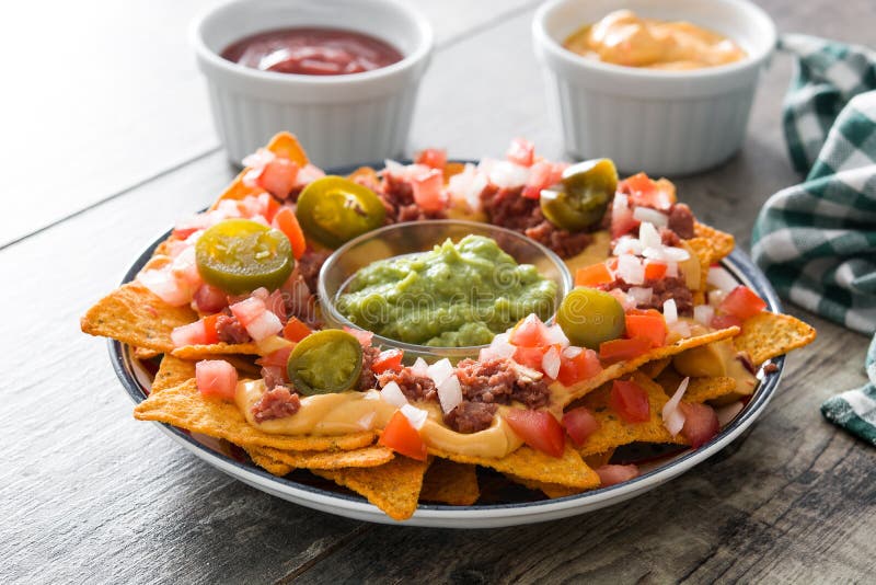 Nacho messicani con manzo, guacamole, la salsa di formaggio, i peperoni, il pomodoro e la cipolla in piatto su legno immagine stock libera da diritti Nacho messicani con manzo, guacamole, la salsa di formaggio, i peperoni, il pomodoro e la cipolla in piatto su legno immagine stock libera da diritti