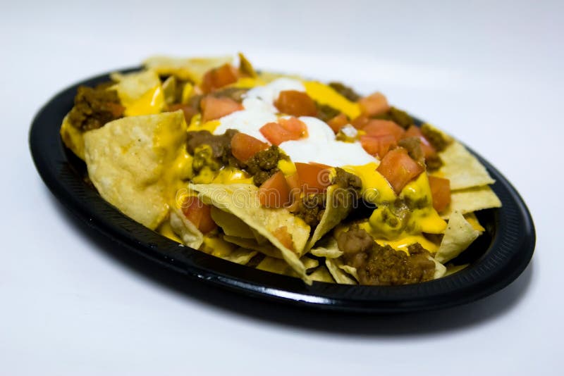 A plate of nachos that has chips, sour cream, tomatoes, cheese and meat