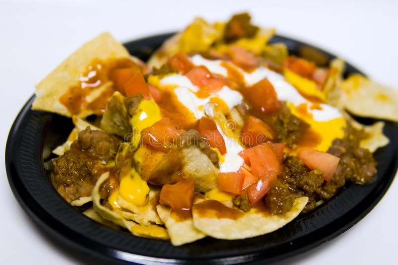 A plate of nachos that has chips, sour cream, tomatoes, cheese and meat