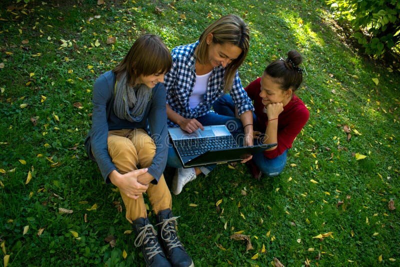 Above view of mother and her teenage children using laptop during autumn day in nature. Above view of mother and her teenage children using laptop during autumn day in nature.