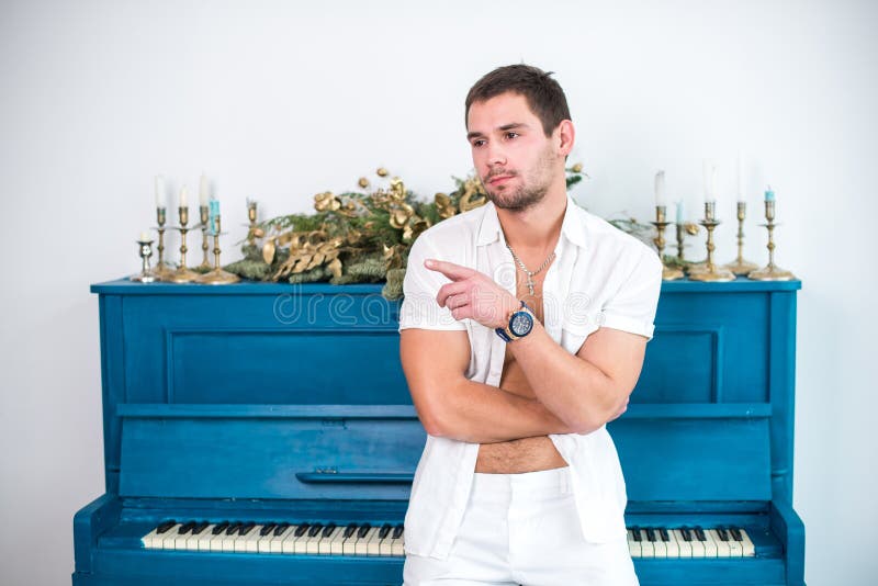 Nadenkende, knappe mens met een baard in witte kleren tegen de achtergrond van een piano, een geraspt overhemd met een naakt tors royalty-vrije stock fotografie Nadenkende, knappe mens met een baard in witte kleren tegen de achtergrond van een piano, een geraspt overhemd met een naakt tors royalty-vrije stock fotografie