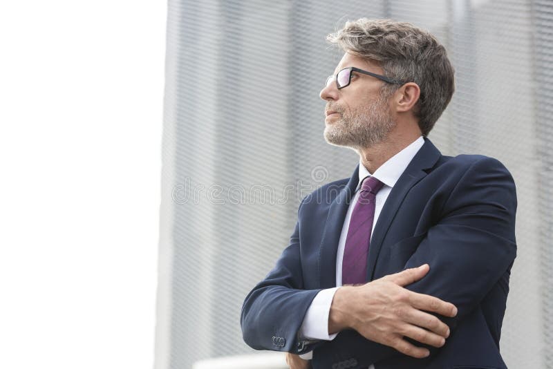 Nadenkende rijpe zakenman die weg terwijl status tegen de bureaubouw kijken royalty-vrije stock fotografie Nadenkende rijpe zakenman die weg terwijl status tegen de bureaubouw kijken royalty-vrije stock fotografie