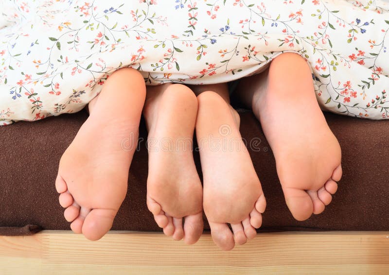 Bare feet of a little girl and boy - kids lying under the blanket with flowers with the small feet of a girl in the middle. Bare feet of a little girl and boy - kids lying under the blanket with flowers with the small feet of a girl in the middle