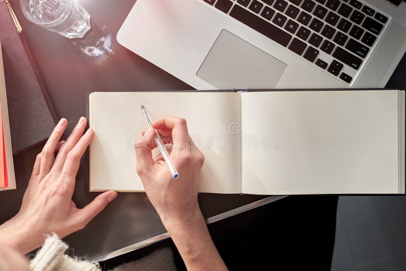 Nah oben von den Händen der Frau, die Anmerkungen auf weißem verbreitetem Buch machen Junge Frau oder Student, die an Papiernotiz lizenzfreie stockfotografie
