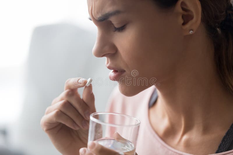 Nahaufnahme der Stirnrunzelnfrauen-Holdingpille und Glas Wasser