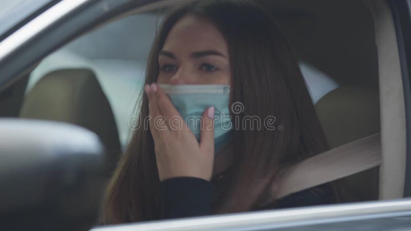 Nahaufnahme des Husten der jungen Frau, die auf tragender Schutzmaske des Fahrersitzes sitzt Porträt der müden brunette Frau mit