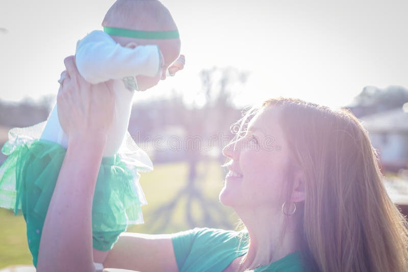 Nahaufnahme des lächelnden anhebenden Babys der Frau oben in helles Sonnenlicht lizenzfreies stockfoto Nahaufnahme des lächelnden anhebenden Babys der Frau oben in helles Sonnenlicht lizenzfreies stockfoto