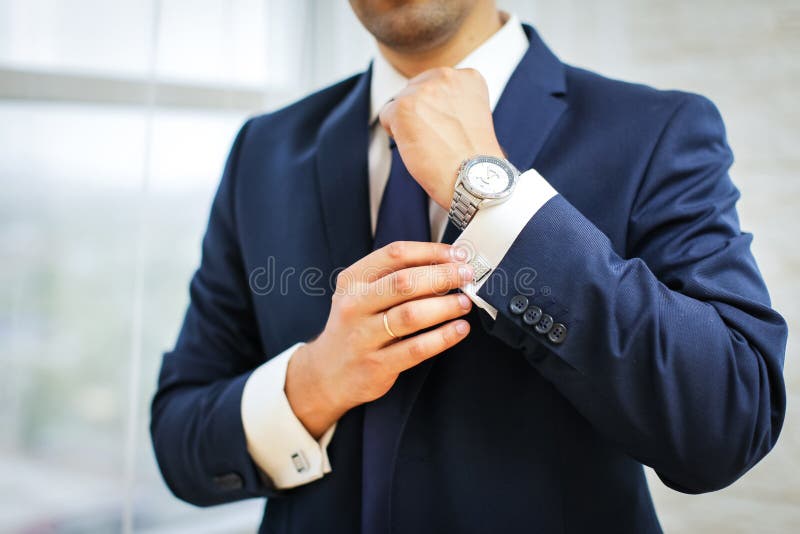 Nahaufnahme des Mannes in der Klage mit Uhr auf seiner Hand, die seinen Manschettenknopf repariert Bräutigamfliegenmanschettenknö stockbild Nahaufnahme des Mannes in der Klage mit Uhr auf seiner Hand, die seinen Manschettenknopf repariert Bräutigamfliegenmanschettenknö stockbild