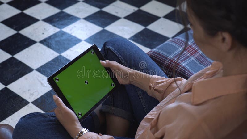 Nahaufnahme einer hübschen jungen Frau, die auf dem Stuhl sitzt und mit einem grüngrüngrüngrüngrüner Bildschirm auf dem Tablett m