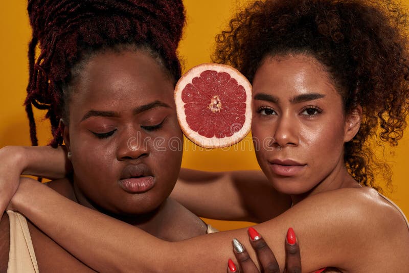 Nahaufnahme eines Porträts zweier ernsthafter junger afrikanischer Amerikanerinnen, die die Hälfte saftiger Grapefruit zwischen si lizenzfreie stockbilder