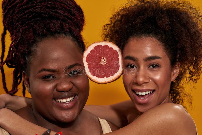Nahaufnahme eines Porträts zweier lächelnder junger afrikanischer Amerikanerinnen, die die Hälfte saftiger Grapefruit zwischen sic lizenzfreies stockfoto